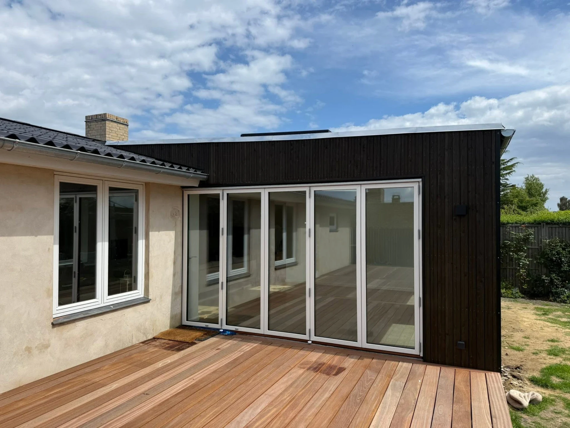 Udendørs terrasse med store glasdøre og trædæk.