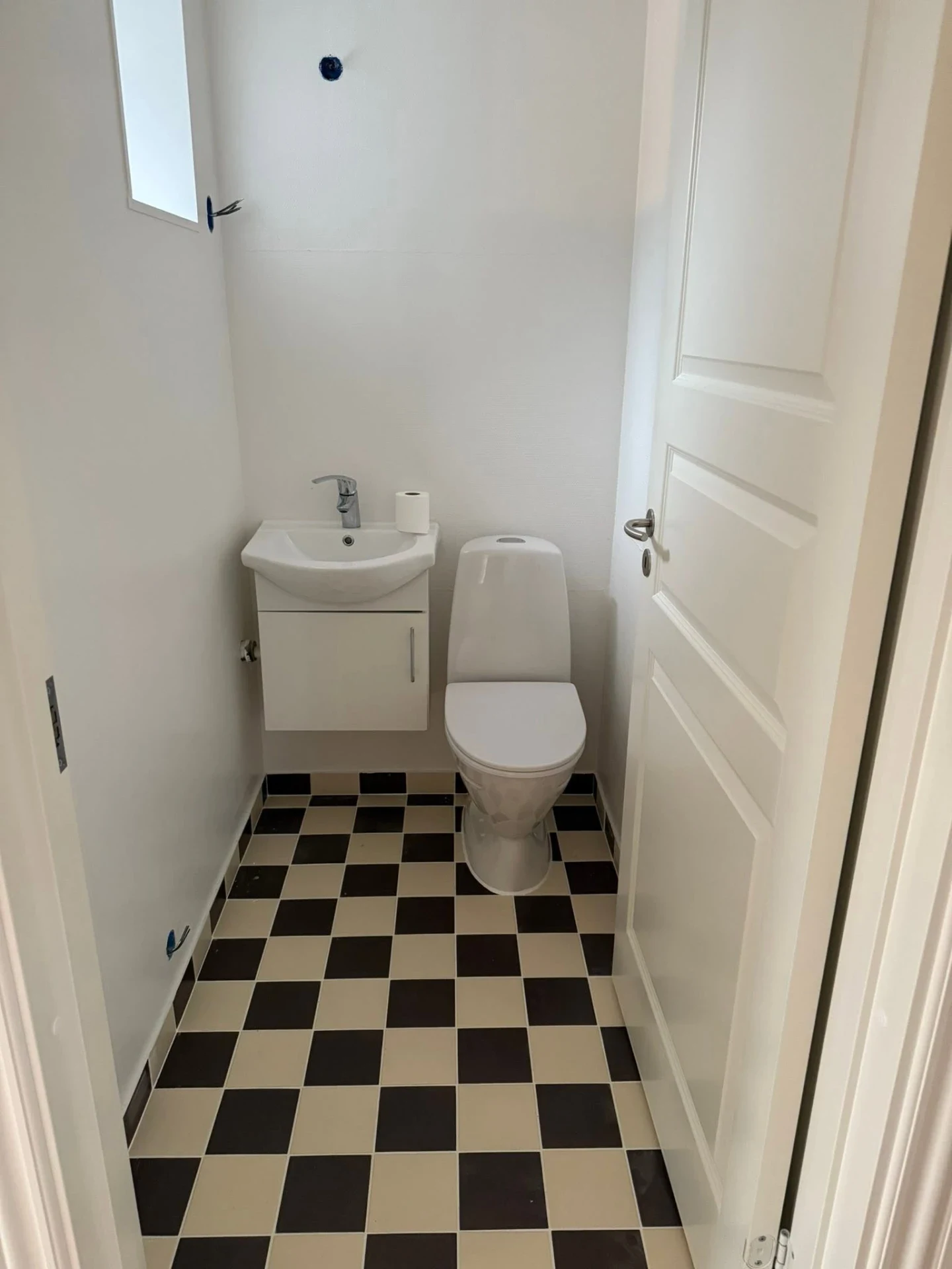 Lille badeværelse med toilet, vask og sort-hvidt flisegulv.