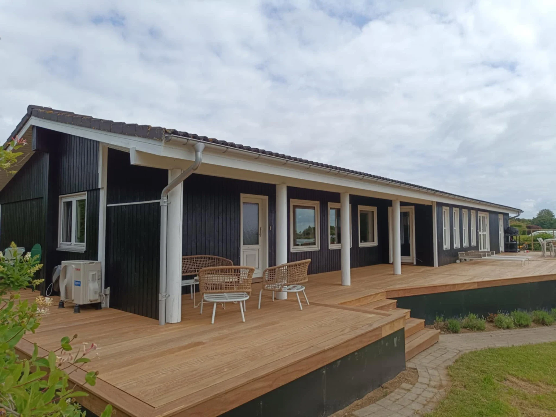 Moderne træhus med stor udendørs terrasse og grønne omgivelser.